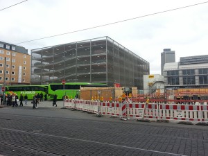 Links die markant-grünen Flixbusse, dahinter das neue Parkhaus. Rechts im Bild im Hintergrund das Hallendach des Hauptbahnhofs und davor die tiefe Baugrube des künftigen Hotels. Etwa in Höhe des weißen Containers wird künftig der Durchgang zwischen Bahn und Fernbus sein.